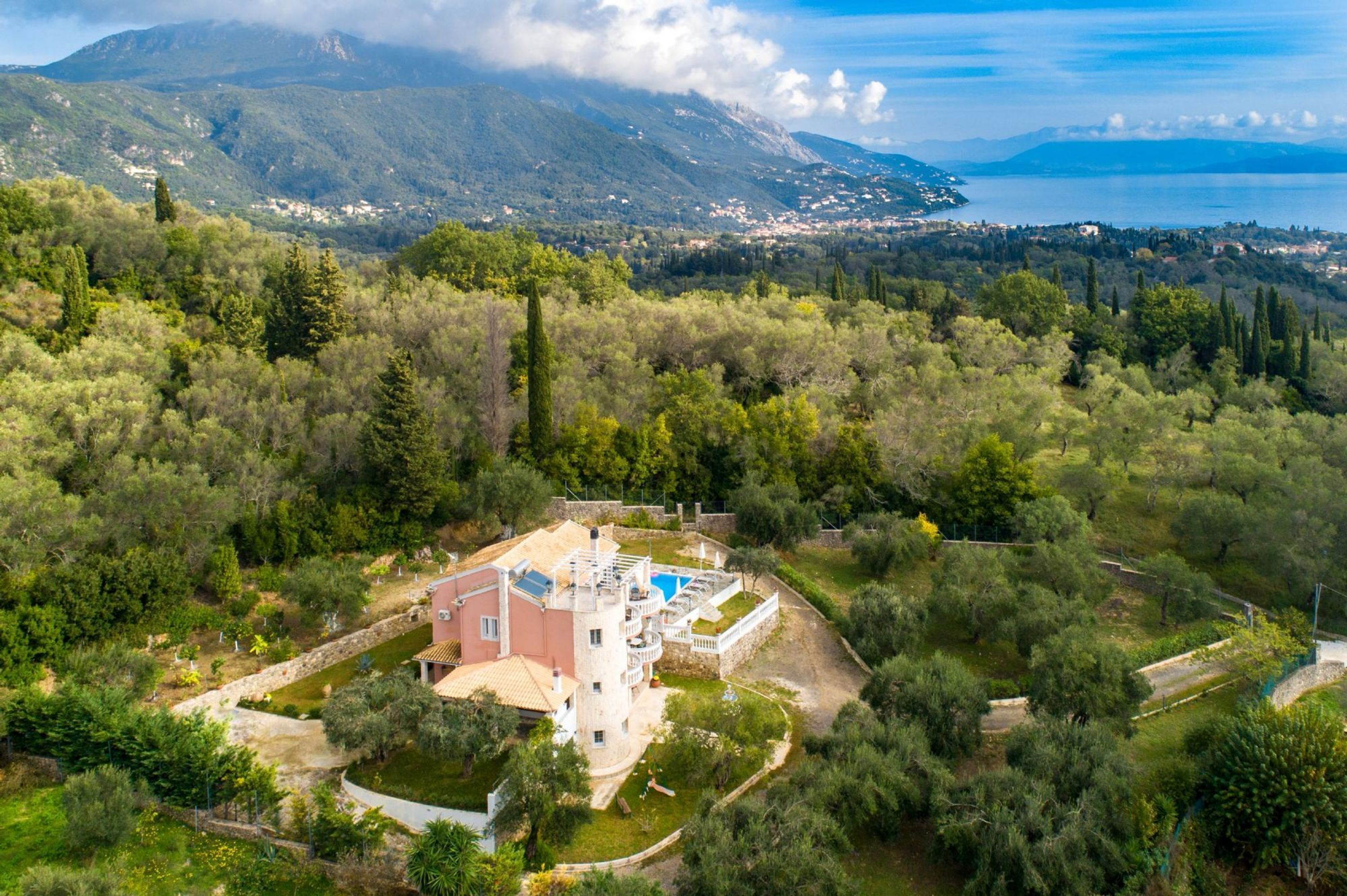 A villa with a pool, surrounded by lush greenery and mountains in the background.