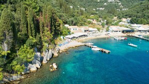 Una zona costiera con acque cristalline turchesi, un molo con barche e una piccola spiaggia con ombrelloni.