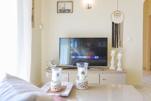 A living room with a flat-screen TV, decorative candle holders, a dreamcatcher, and a framed picture on the wall. - Villa Seasunrise in Perama (Koroni)