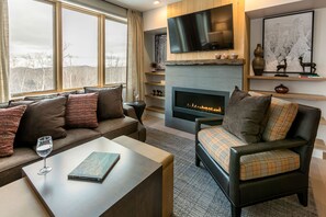 A modern living room with a fireplace, a sofa, a chair, and a coffee table. - Okemo Mountain 4BR Ski-In Condo | Sleeps 12! (Ludlow)