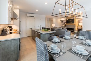 Eine moderne Küche mit integrierter Kochinsel, ein Essbereich mit gedeckten Tischen und ein Wohnzimmer mit Kamin.