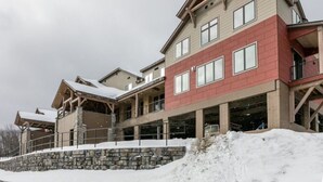 A multi-story building with a stone base, wooden balconies, and large windows. - 5BR Ski-In Condo in Okemo Mountain | Near Lifts! (Ludlow)