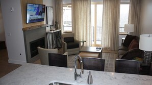 Una habitación de hotel moderna con cocina, chimenea, televisor de pantalla plana y balcón con cortinas.