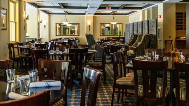 Un restaurante con varias mesas y sillas, una alfombra estampada y luces en el techo.