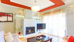 Una sala de estar con un sofá, una mesa de centro, una chimenea, un televisor y un ventanal con cortinas.
