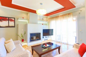 Ein Wohnzimmer mit einer Couch, einem Couchtisch, einem Kamin, einem Fernseher und einem großen Fenster mit Vorhängen.