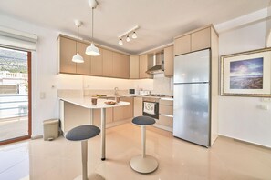 A modern kitchen with a central island, pendant lights, and a stainless steel refrigerator. - Villa Elmas in Kalkan (Kalkan Belediyesi)