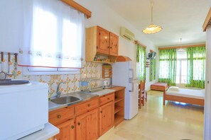 A compact kitchen with wooden cabinets, a refrigerator, and a dining area with a table and chairs. - Faros Tria in Gaios with 1 bedrooms and 1 bathrooms (Gaios)