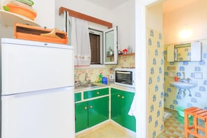 Eine kleine Küche mit grünen Schränken, einem weißen Kühlschrank und einer Mikrowelle.
