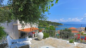 Una terrazza con pavimento in pietra, poltrone bianche e un'ampia pianta in vaso.