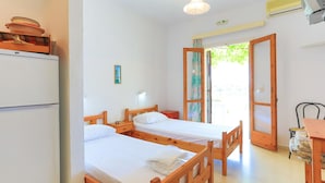 Una habitación con dos camas de madera, una mesita, una silla, un refrigerador y una ventana con vistas a zonas verdes.
