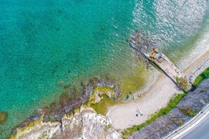 An aerial view of a coastal area with clear turquoise water, rocky shorelines, and a paved walkway along the beach. - Mouragia House in Kerkira (Kerkira)