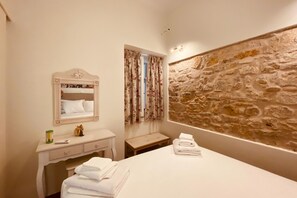 A bedroom with a bed, a dresser, a mirror, a stone wall, and a window with curtains. - Mouragia House in Kerkira (Kerkira)