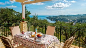 Una terraza con una mesa preparada para comer, con vistas a un paisaje pintoresco con árboles y el mar.