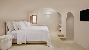 Ein schlicht eingerichtetes Schlafzimmer mit einem großen Bett, einem kleinen Nachttisch und einem fest installierten Fernseher.
