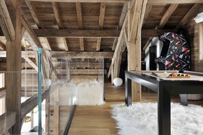 A wooden interior with a pool table, white furry ottomans, and a glass-enclosed area.