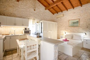 A compact kitchen with white cabinets, a dining table, and a bed with a nightstand. - Korinas Cottage in Kentroma (Kentroma)