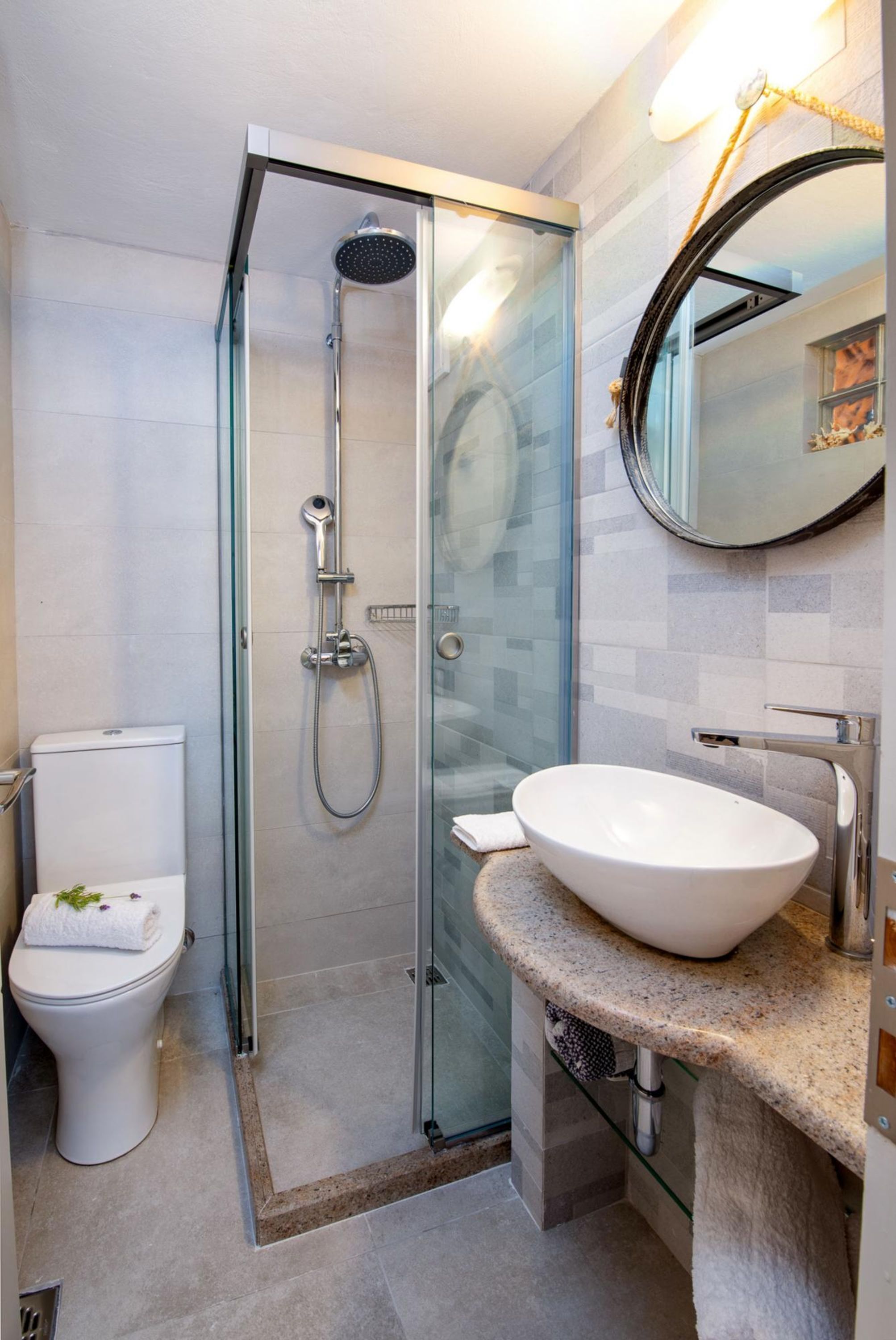 Un baño moderno con ducha envuelta en vidrio, inodoro blanco y un lavamanos grande con espejo superior.
