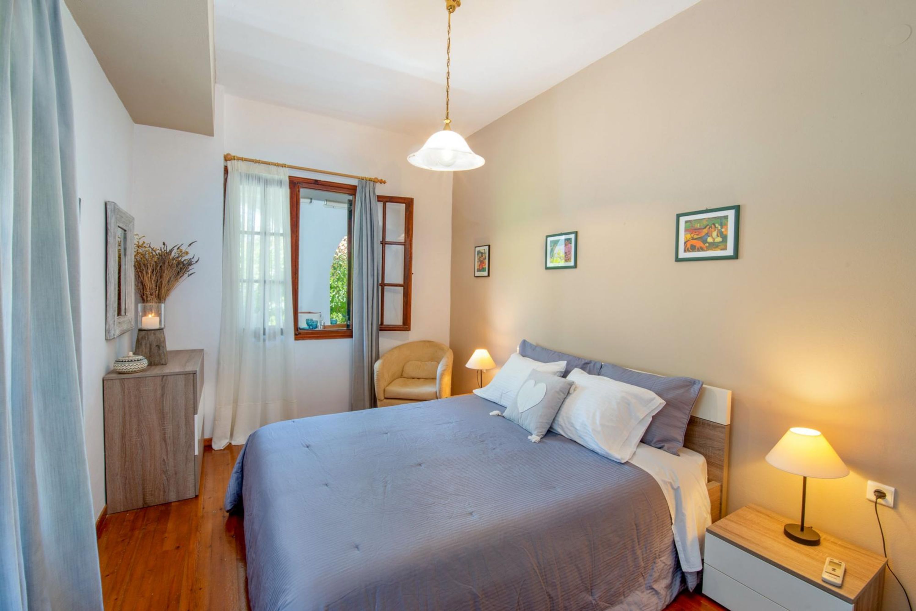 Une chambre à coucher avec un grand lit, une table de chevet avec une lampe, une chaise et une fenêtre avec des rideaux.