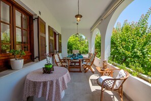 A covered outdoor seating area with a table and chairs, surrounded by potted plants and a view of greenery. - Villa Eleni Paxos in Gaios (Gaios)