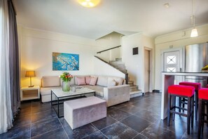 Ein modernes Wohnzimmer mit einer Couch, einem Hocker und einem Couchtisch, einer Treppe und einer Küchenzeile mit roten Barhocker.