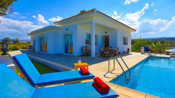 Una casa moderna con piscina, sillas reclinables azules y un patio con mobiliario exterior.