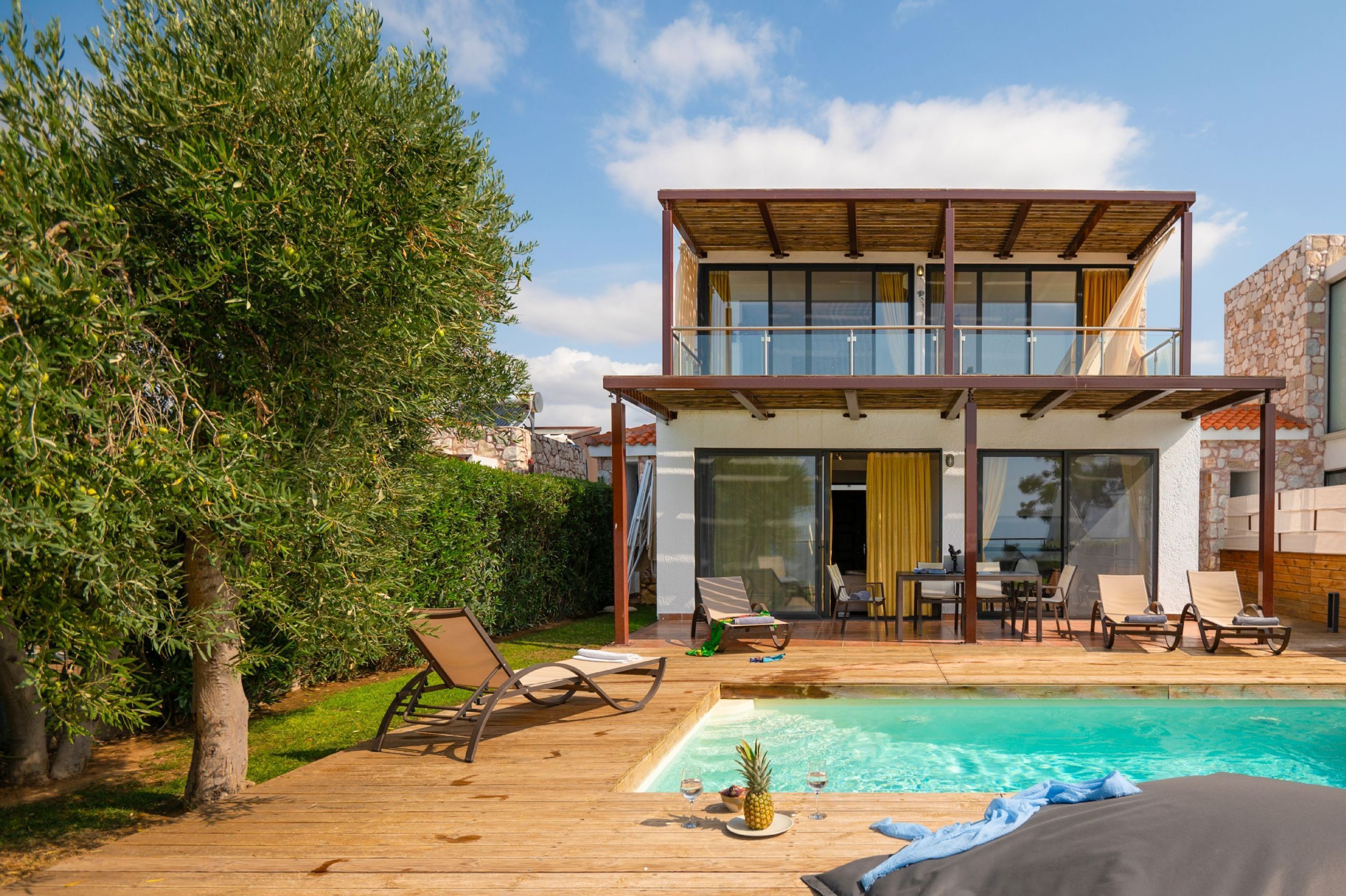 A modern two-story house with a swimming pool, deck chairs, and a dining area.