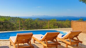 Zona junto a la piscina con tres sillas de madera y vista despejada al océano.