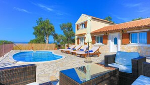 Zona junto a la piscina con sillas de descanso, piscina y terraza de piedra.