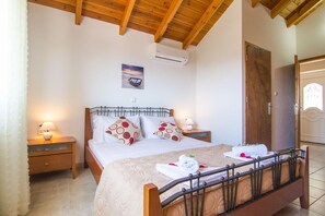 Ein Schlafzimmer mit Holzboden, einem Bett mit beige farbenem Überwurf, zwei Kissen mit Punkten, einem Nachttisch mit Lampe und einer Klimaanlage an der Wand.