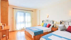 A hotel room with two beds, wooden flooring, a desk, and a window with curtains. - Villa Eos in Kalkan with 3 bedrooms and 4 bathrooms (Kalkan)