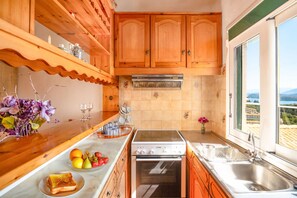 A kitchen with wooden cabinets, a stove, a dishwasher, and a window with a view. - The Old Office in Kalami (Kalami)