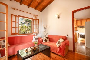 A cozy living room with a wooden ceiling, a red sofa with patterned cushions, a glass coffee table, and a view of the outside through a window with wooden shutters. - The Old Office in Kalami (Kalami)