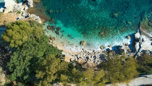 Vista aérea de una zona costera con aguas turquesas cristalinas, costa rocosa y densa vegetación verde.