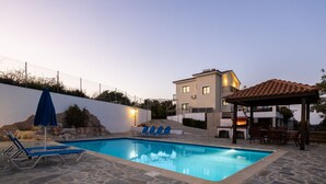 Ein Swimmingpool mit Liegestühlen und einer Grillanlage, umgeben von Steinplatten und einer weißen Mauer.