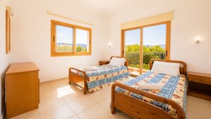 Ein Schlafzimmer mit zwei hölzernen Betten, einem Nachttisch aus Holz, einer kleinen Holzkommode und großen Fenstern mit Blick.