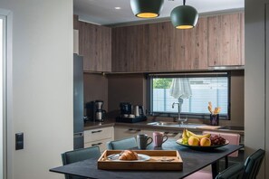 A modern kitchen with wooden cabinets, a dining table with chairs, a coffee maker, and a fruit bowl. - Villa Amo With Private Pool (Heraklion)