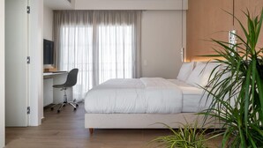 Ein modernes Hotelzimmer mit einem großen Bett, einem Schreibtisch mit Stuhl und einem großen Fenster mit Vorhängen.