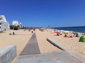 A beach with a wooden walkway leading to the water, umbrellas, and beach chairs. - T0 A/C Varandas Mar 3ºB perto PRAIA Wi-Fi (Quarteira)
