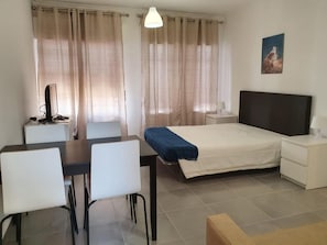 A hotel room with a bed, a desk with a computer, a chair, a bedside table with a lamp, and a painting on the wall. - T0 A/C Varandas Mar 3ºB perto PRAIA Wi-Fi (Quarteira)