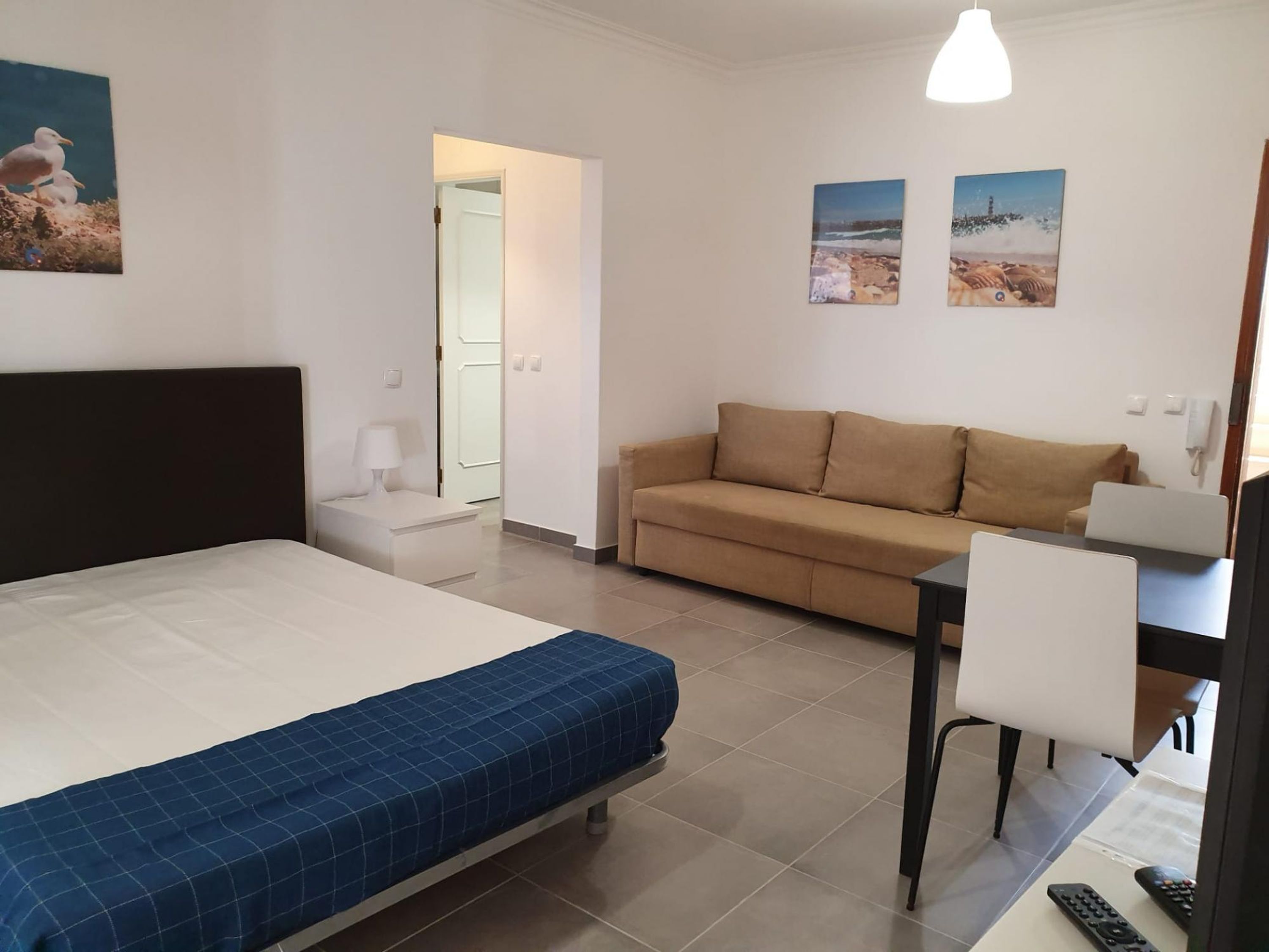 A hotel room with a bed, a sofa, a desk with a chair, and two paintings on the wall.