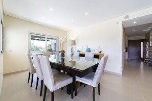 A modern dining area with a glass table, six chairs, and a vase of flowers. - Maria in Albufeira with 6 bedrooms and 5 bathrooms (Albufeira)