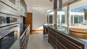 Eine moderne Küche mit Edelstahlgeräten, einem Esstisch mit Glasplatte und Blick auf einen Pool und Sitzgelegenheiten im Freien.