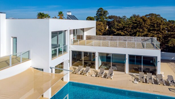 Ein modernes, zweistöckiges Gebäude mit Pool, Liegestühlen und einem Glasgeländer.