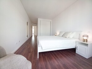 A bedroom with a large bed, a nightstand, a chair, and a wardrobe. - T3 Alto Forte -Vista Mar,Ar Condicionado,Garagem (Quarteira)