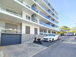A multi-story residential building with balconies, a covered garage, and a parked white car. - T3 Alto Forte -Vista Mar,Ar Condicionado,Garagem (Quarteira)