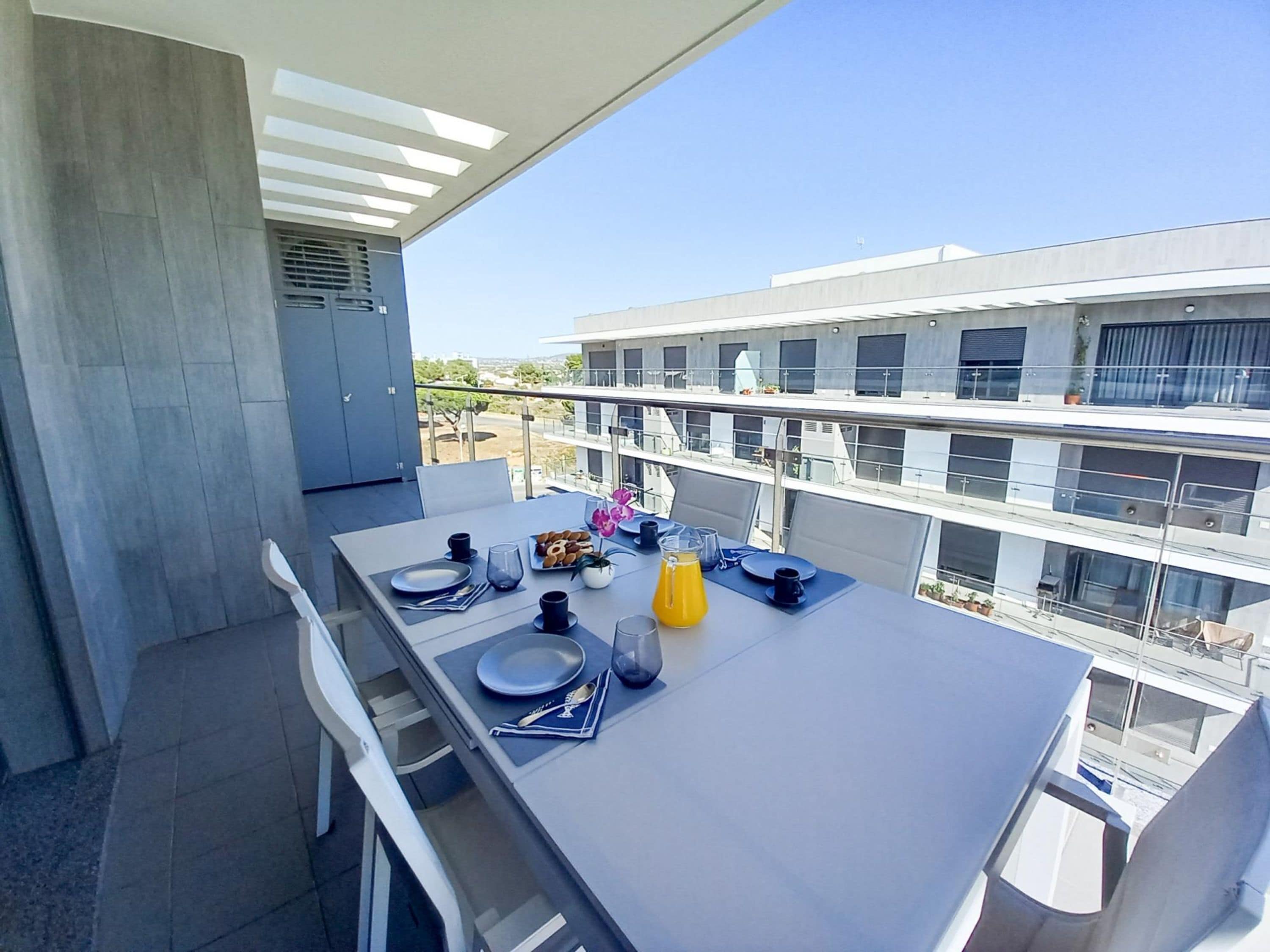 A balcony with a dining table set for two, equipped with plates, cutlery, and a glass of orange juice.