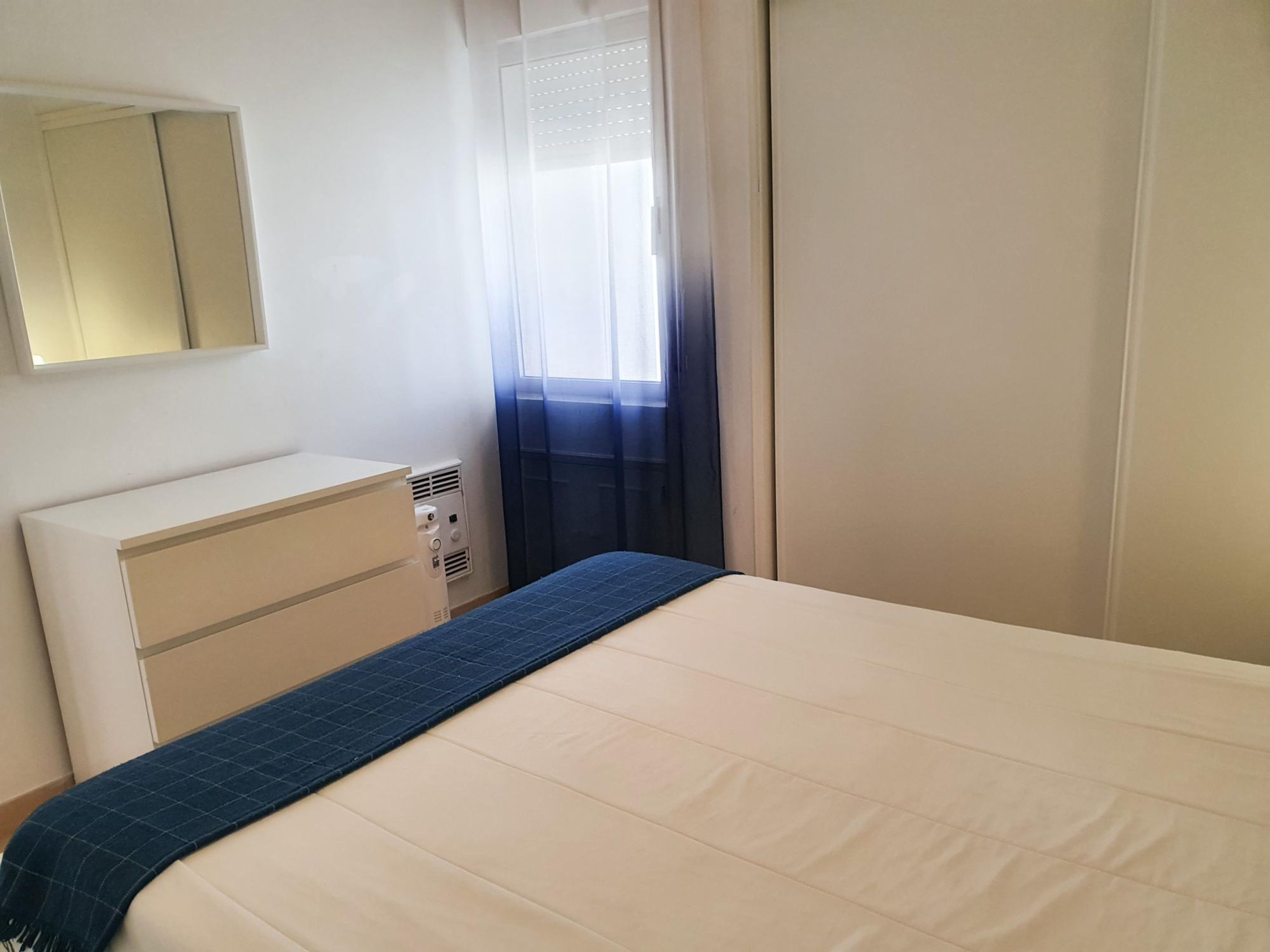 Un dormitorio con cama, cómoda, espejo y ventana con cortinas.