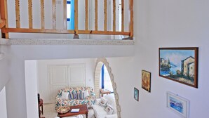 A two-level interior with a wooden balcony railing, a patterned sofa, and artwork on the walls. - Villa Mandola Rosa in Poli Crysochous (Poli Crysochous)
