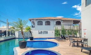 Un área de piscina con varias piscinas, sillas de descanso y un edificio identificado como 'Lavitta Residences | Beach and Park'.